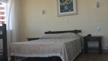 A bedroom with a bed, a nightstand, a bedside table, a painting on the wall, and a window with curtains.