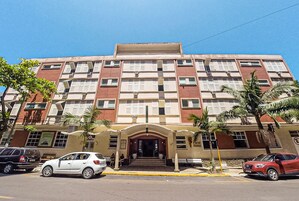 Un hotel de varios pisos con entrada central, balcones y un estacionamiento al frente.