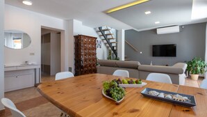 A modern living room with a wooden dining table, a sofa, a TV mounted on the wall, and a staircase leading to another level. - Family villa Nicole in Štinjan (Štinjan)
