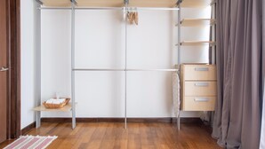 Een inloopkast met open planken, een kledingroede en een klein tafeltje met een mand.