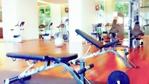 Een sportschool met fitnessapparatuur, een halterbank en een spiegelwand.