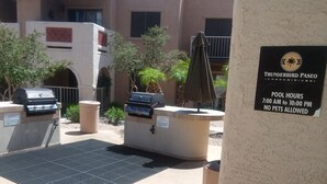 Espaço de pátio externo com churrasqueiras, área de estar coberta e placa com horários da piscina e política de animais de estimação.