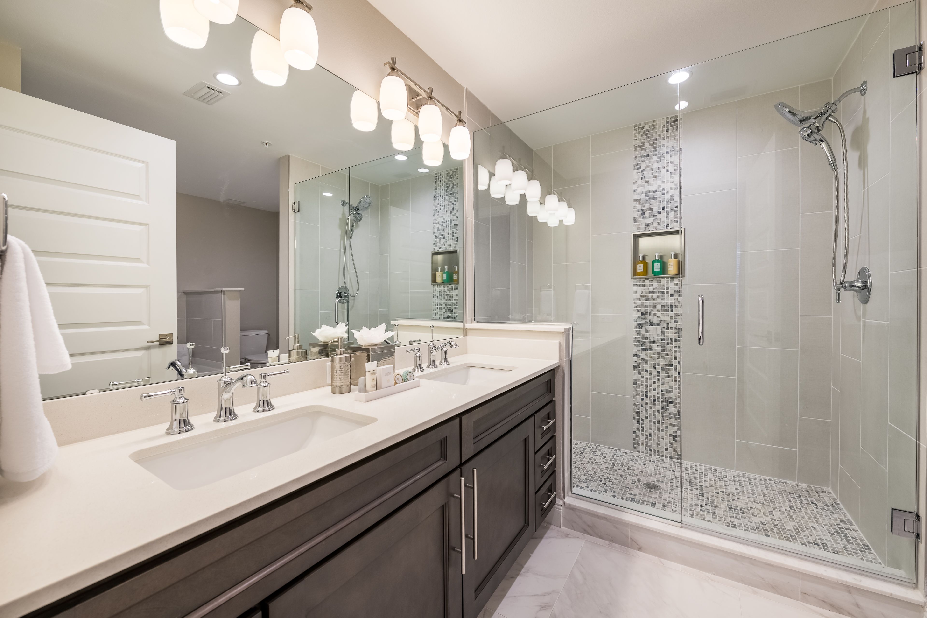 A modern bathroom with a large mirror, two sinks, a shower, and a glass-enclosed shower area.