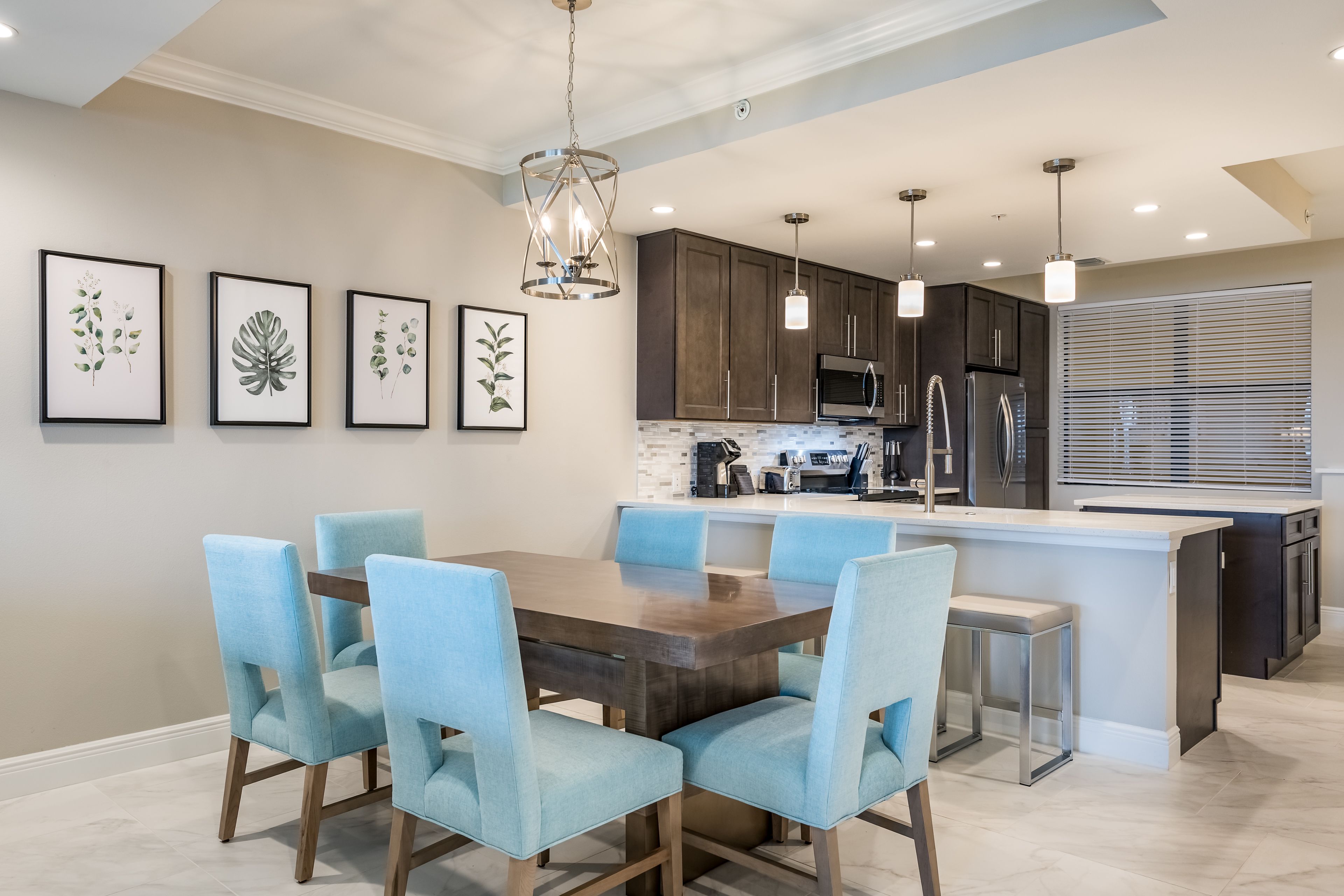 Una cocina moderna con armarios de madera oscura, una isla central con taburetes altos y una mesa de comedor con sillas tapizadas en azul claro.