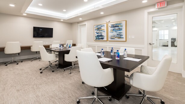 A conference room with a long table, white chairs, a flat-screen TV, and two framed artworks on the wall. - Siena at Bella Collina (Montverde)