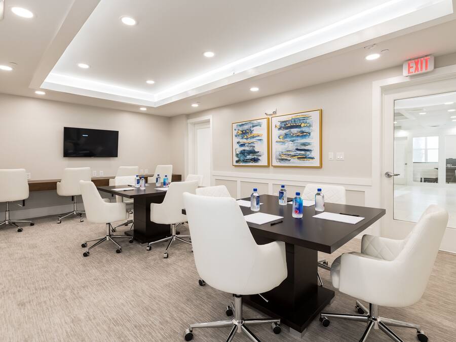 A conference room with a long table, white chairs, a flat-screen TV, and two framed artworks on the wall.