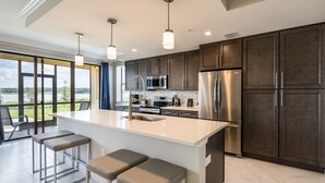 Une cuisine moderne dotée d’un grand îlot central, d’appareils électroménagers en acier inoxydable et offrant une vue sur l’extérieur.