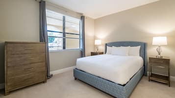 A bedroom with a large bed, a dresser, two bedside tables with lamps, and a window with blinds.