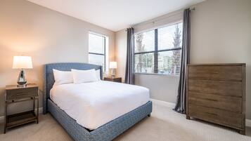 A bedroom with a large bed, two bedside tables with lamps, a dresser, and a window with blinds.
