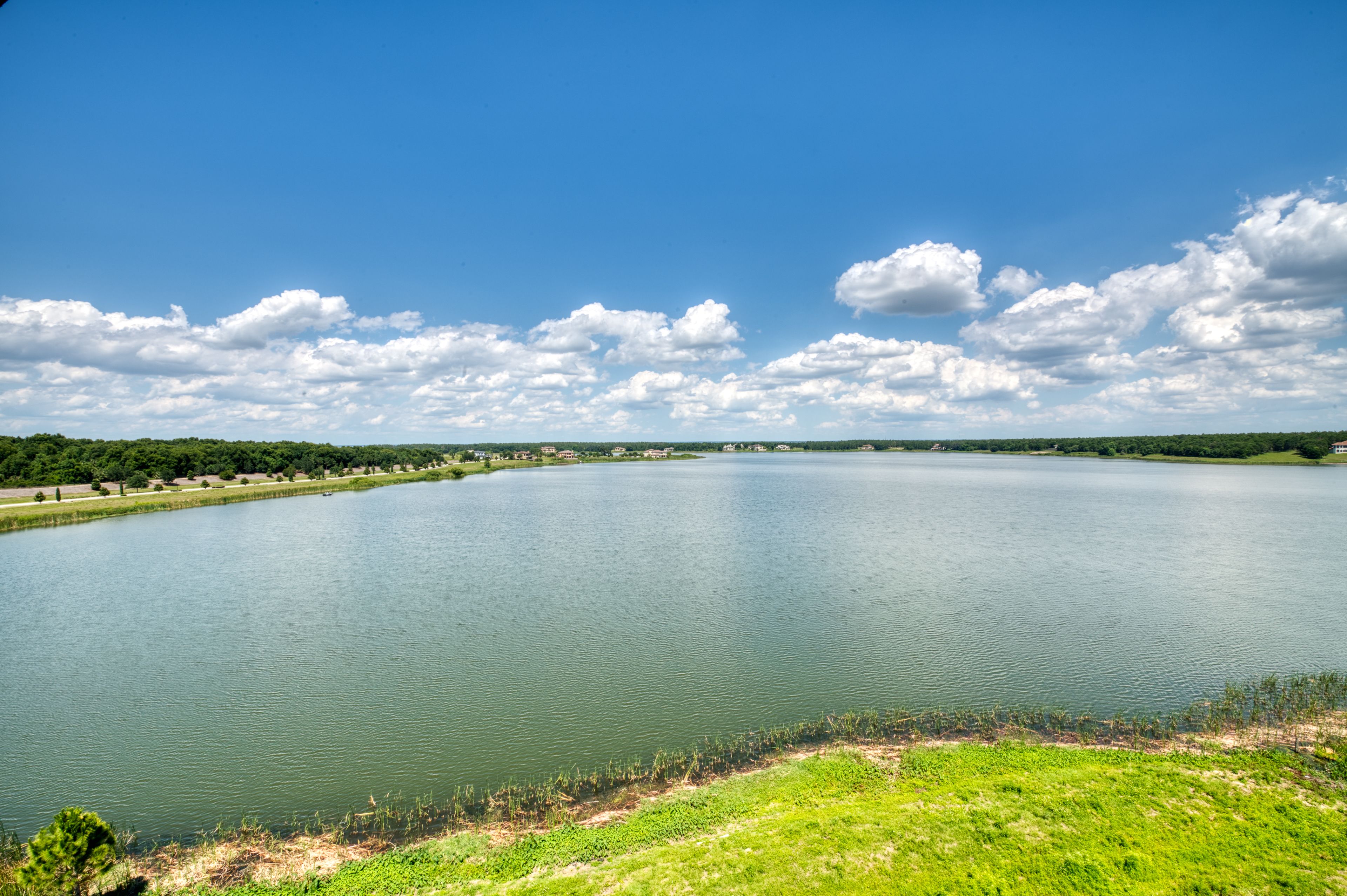 A large lake with a grassy shoreline and a clear blue sky with clouds.