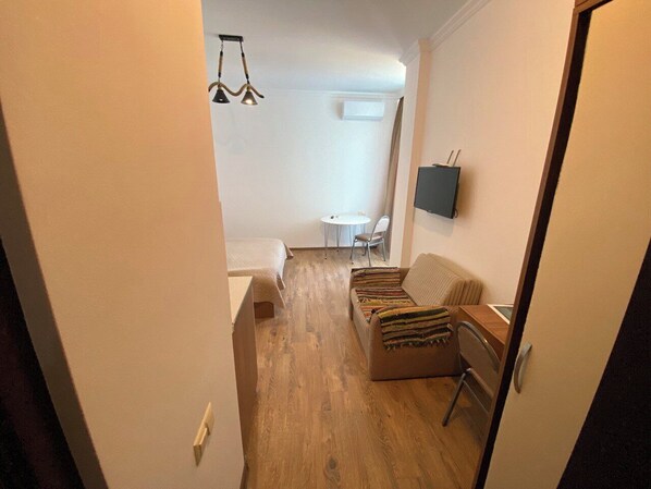 Una habitación compacta con una cama, un sofá, una mesita pequeña y un televisor fijado a la pared.