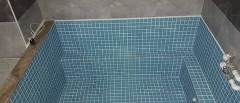 A rectangular bathtub with blue mosaic tiles, a drain, and a pipe on the right side.