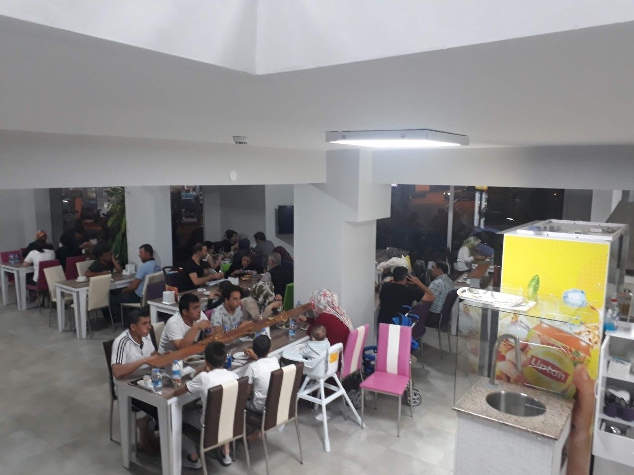 A cafeteria with multiple tables and chairs, people dining, and a vending machine.