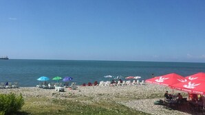 Une plage bordée de rangées de transats et de parasols, un rivage rocheux et une mer calme.