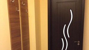Un couloir avec un banc en bois, une porte noire ornée d’un motif abstrait blanc et deux panneaux en bois sur le mur.