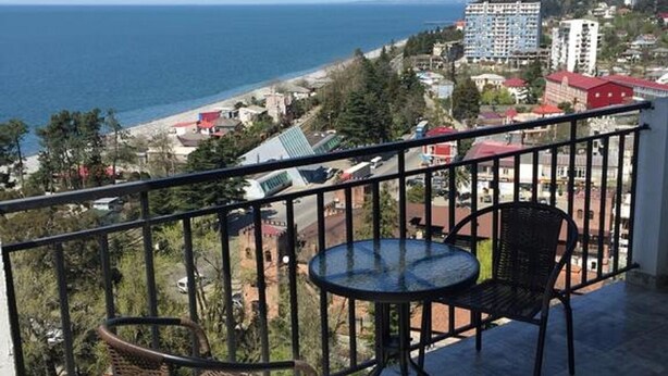Un balcon avec deux fauteuils en osier et une petite table ronde, offrant une vue sur la côte, avec des bâtiments et une plage.