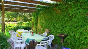 Une terrasse extérieure avec une table et des chaises, abritée par une pergola et entourée de verdure.