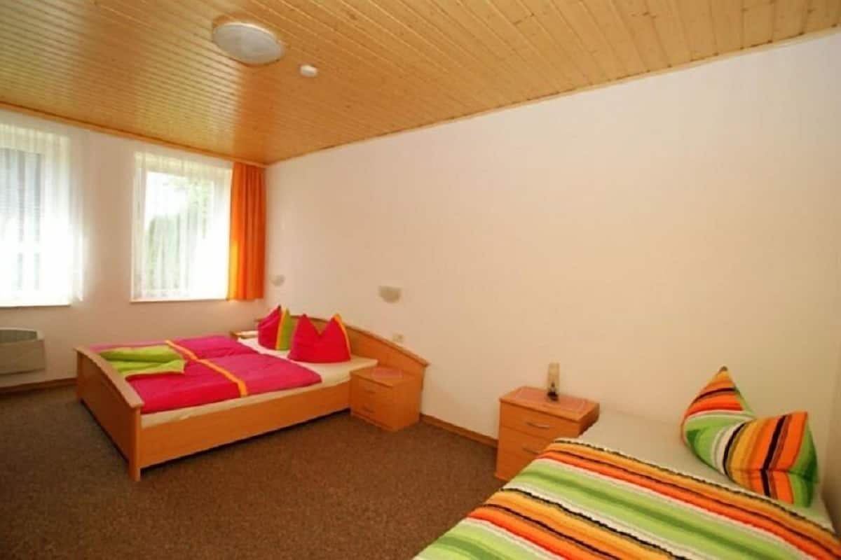 A bedroom with a wooden bed, a nightstand, a bedside table, and a window with curtains.
