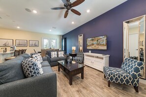 A living room with a dark blue wall, a ceiling fan, a sofa with patterned cushions, a coffee table, and a patterned armchair.
