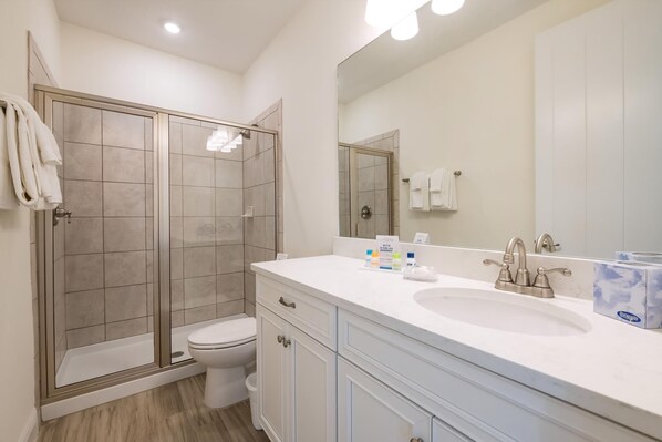 Un baño moderno con ducha de vidrio, inodoro, lavamanos con espejo y toallero.