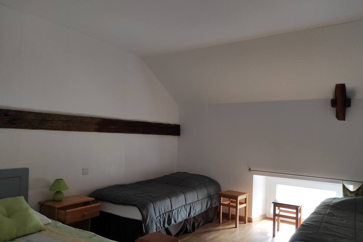 A bedroom with a bed, a nightstand, a desk, and a window.