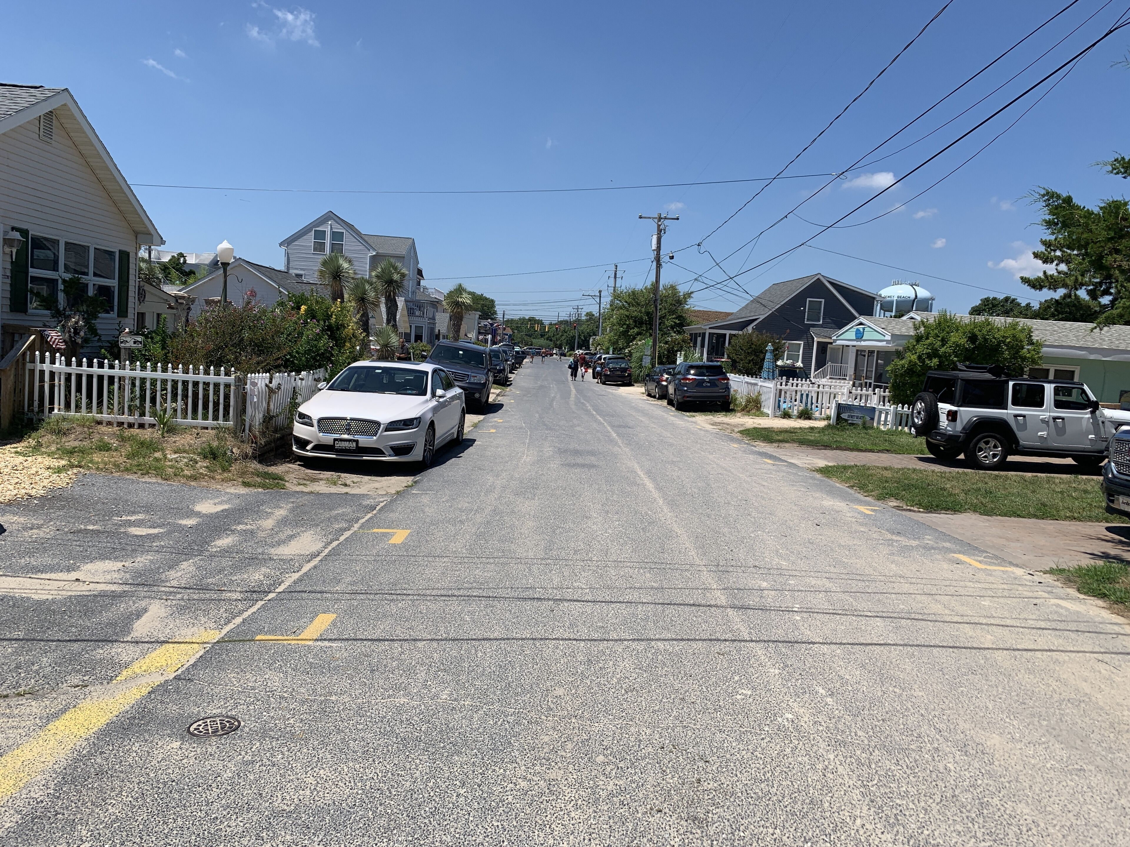 A residential street lined with houses, parked cars, and a clear sky.