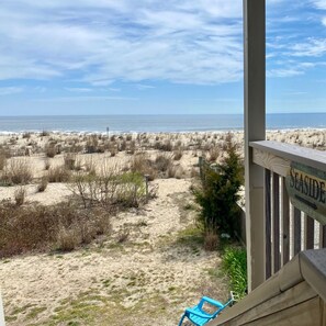 A beach view from a porch with a 'SEASIDE' sign, sandy dunes, and sparse vegetation. - LOCATION! pet friendly! Oceanfront building! Free Parking! Walk everywhere!!  (Dewey Beach)