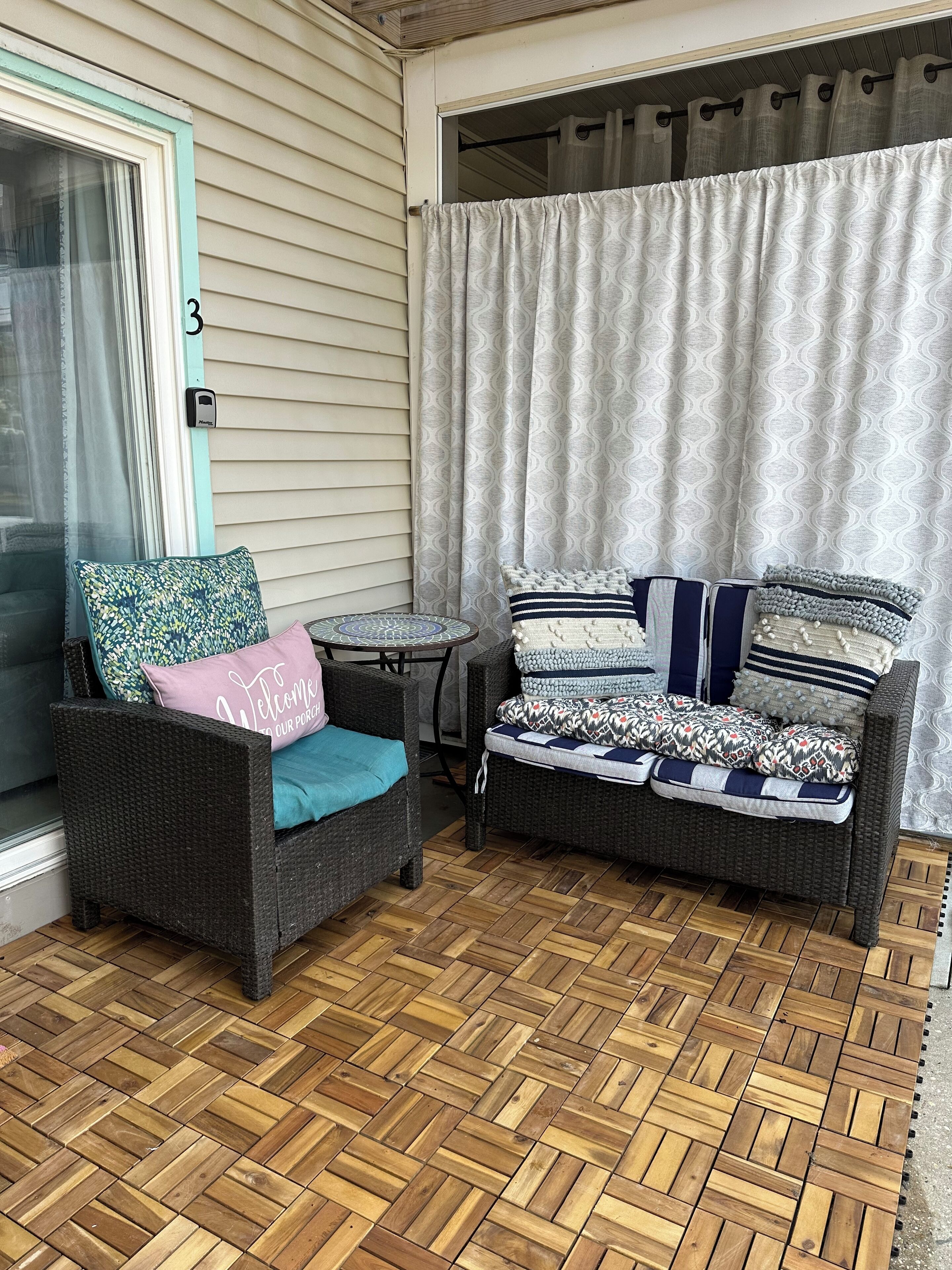A covered patio area with wicker furniture, a small round table, and a patterned curtain.