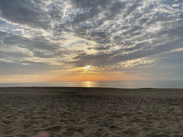 A beach with a wide sandy area and a sunset in the background.