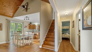 Une pièce spacieuse avec un escalier en bois, un coin repas comprenant une table et des chaises, et une vue sur l’extérieur grâce à une grande fenêtre.