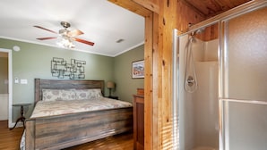 Une chambre avec un lit en bois, un ventilateur de plafond, une douche et une porte en bois.