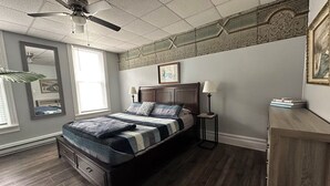 Een slaapkamer met een bed, een plafondventilator, een nachtkastje, een lamp, een kaptafel en een raam.
