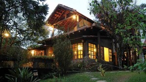 A rustic house with a sloped roof, large windows, and a well-maintained garden with stepping stones and greenery. - Hotel Warabi (Resende)