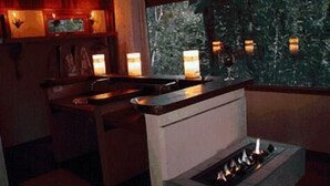 A dimly lit bar area with a fireplace, wooden furniture, and a view of trees through a window. - Hotel Warabi (Resende)