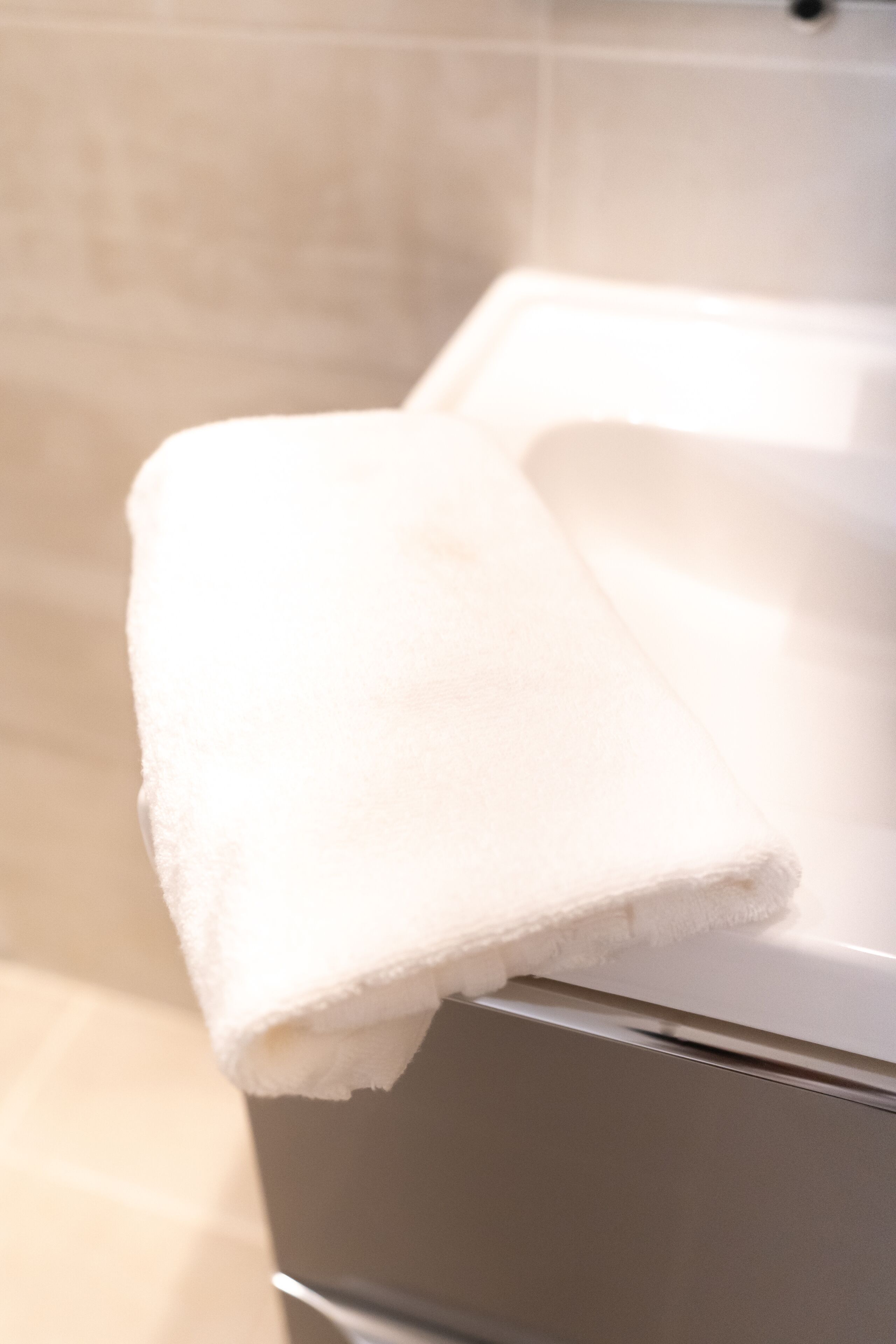 A white towel on a metallic surface, likely a towel warmer, in a bathroom with tiled walls.