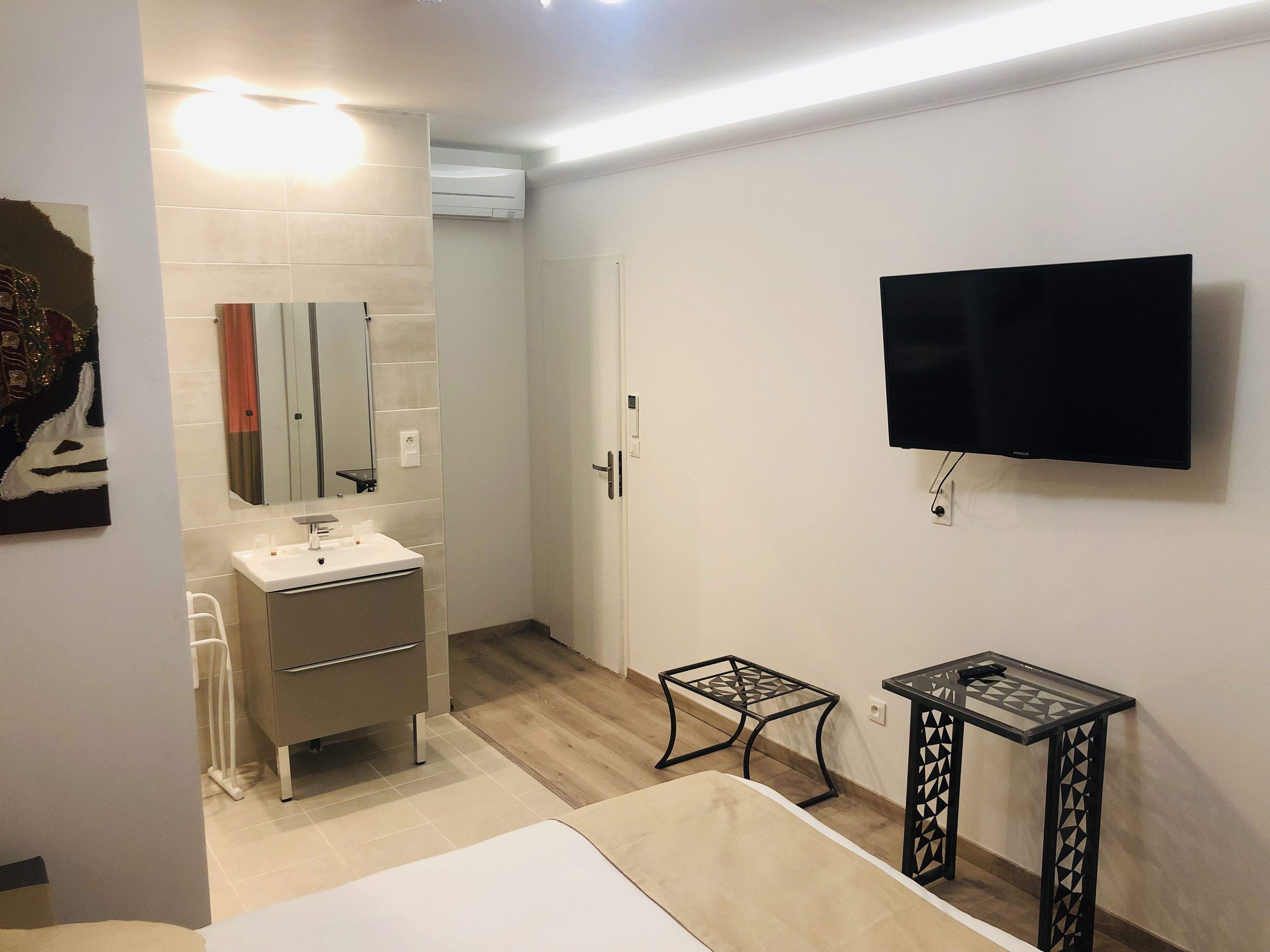 A modern bathroom with a sink, mirror, and toilet. There is a TV mounted on the wall and a small table with a chair.
