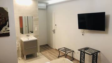 A modern bathroom with a sink, mirror, and toilet. There is a TV mounted on the wall and a small table with a chair.