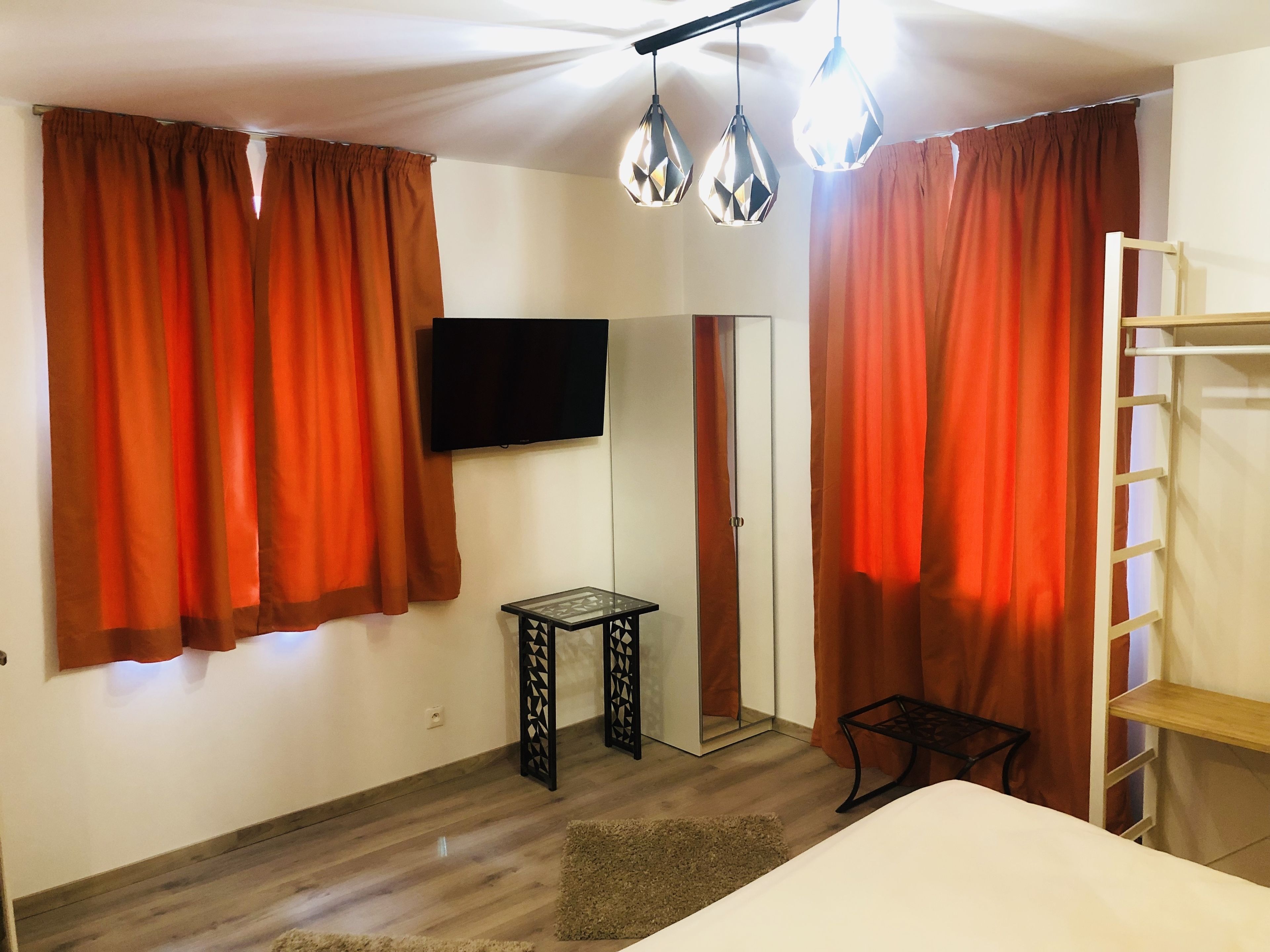 Une chambre à coucher comprenant un lit, un téléviseur fixé au mur, une petite table et une armoire avec un miroir.