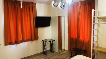 Une chambre à coucher comprenant un lit, un téléviseur fixé au mur, une petite table et une armoire avec un miroir.