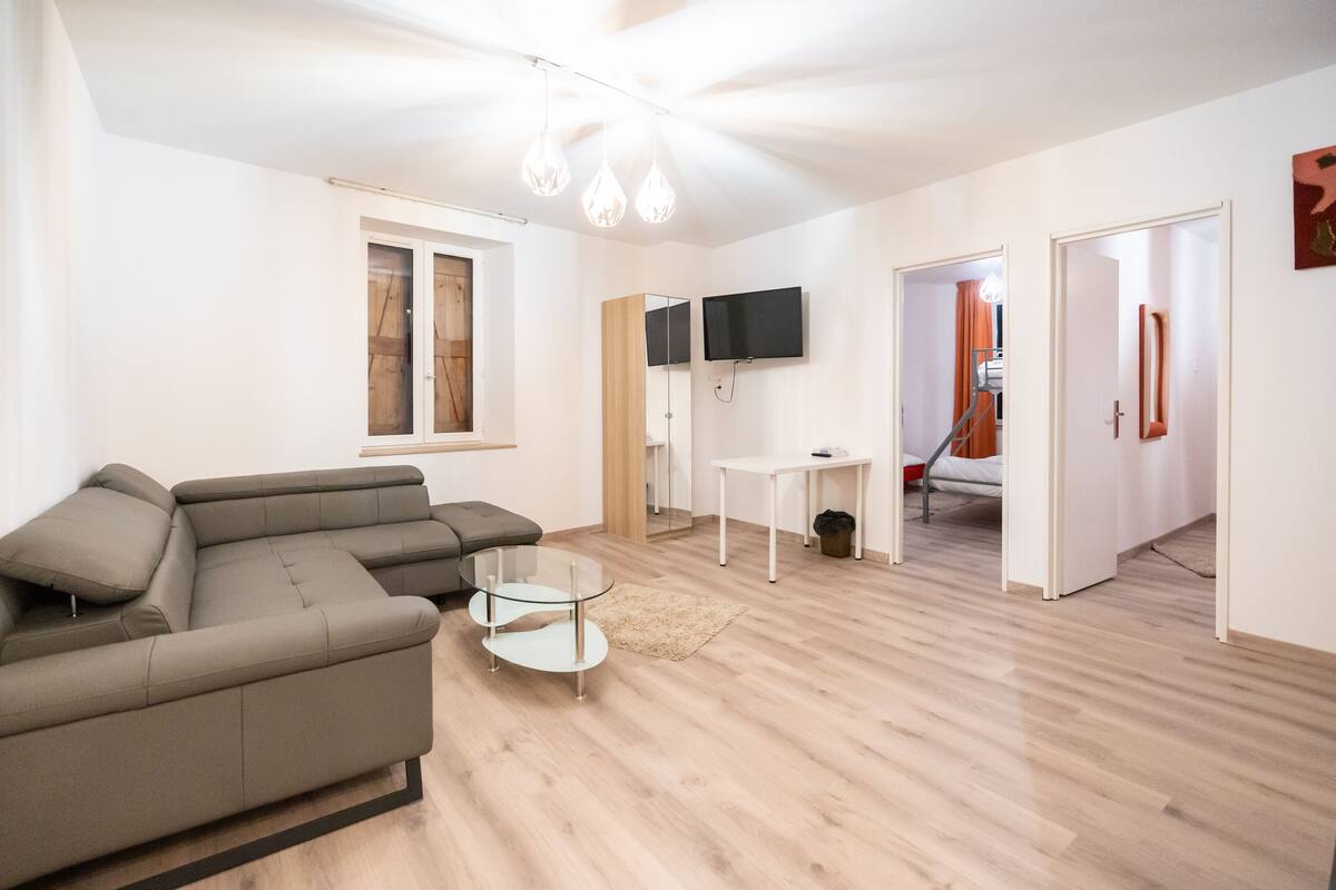 Un salon moderne avec un canapé d’angle, une table basse en verre et un téléviseur à écran plat fixé au mur.