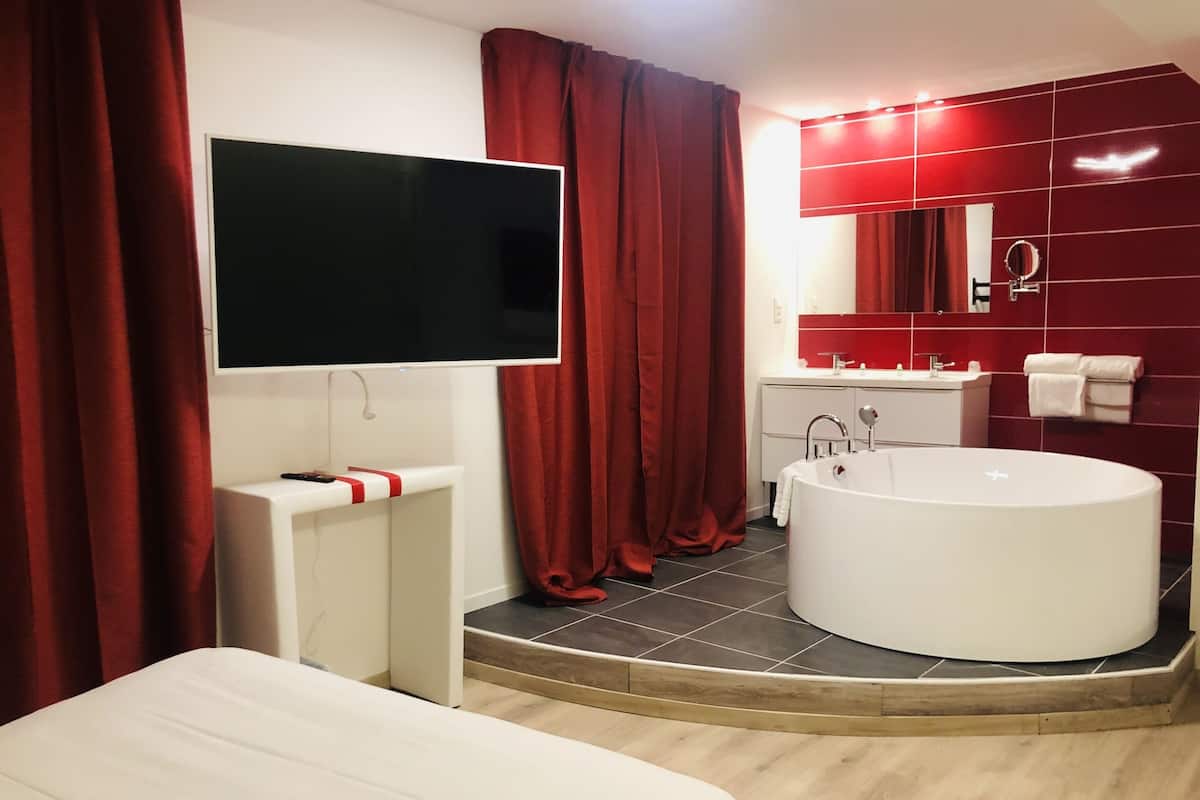 Une salle de bain moderne avec une grande baignoire, un meuble-lavabo avec un miroir et un téléviseur fixé au mur.
