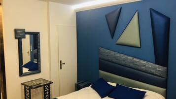 Quarto com cama, mesa de cabeceira, espelho e parede com padrões geométricos.