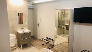 Une salle de bain moderne dotée d’une douche à parois de verre, d’un meuble-lavabo avec miroir et d’un téléviseur à écran plat fixé au mur.