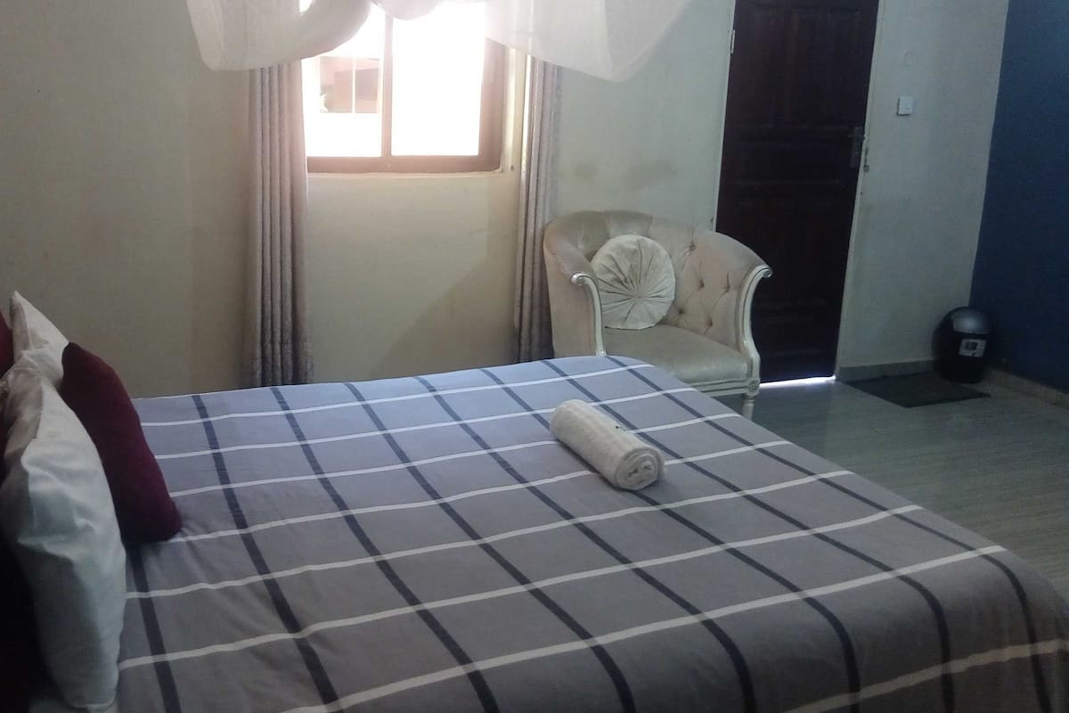 A hotel room with a bed, a chair, a window, and a door.