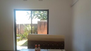 Hotelkamer met een bed, een tafel met twee flessen, en uitzicht op een tuin door een schuifdeur.