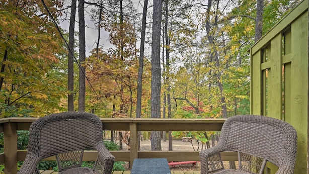 A wooden deck with wicker chairs and a small table, surrounded by trees with autumn foliage.