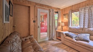 Et hyggeligt rum med træpaneler, en lædersofa, en polstret bænk, et bord med en lampe og en dør, der fører til et andet rum.
