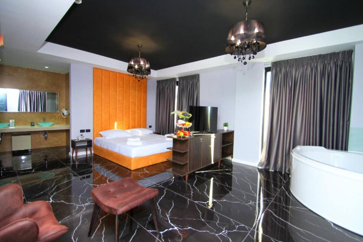 A modern hotel room with a large bed, a sitting area, a TV, and a bathtub.