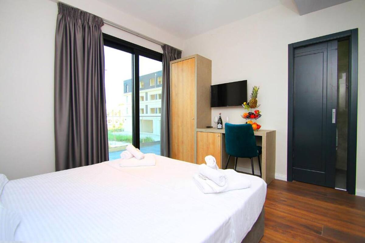 A hotel room with a bed, a desk with a chair, a TV, and a view of the outside.