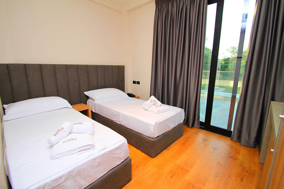 A hotel room with two beds, a grey headboard, and a large window with curtains.